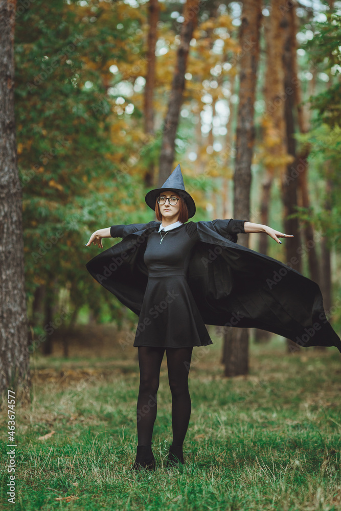 Halloween Witch. Portrait of a girl in a hat and a witch costume in the forest. Ready for trick or treat holiday