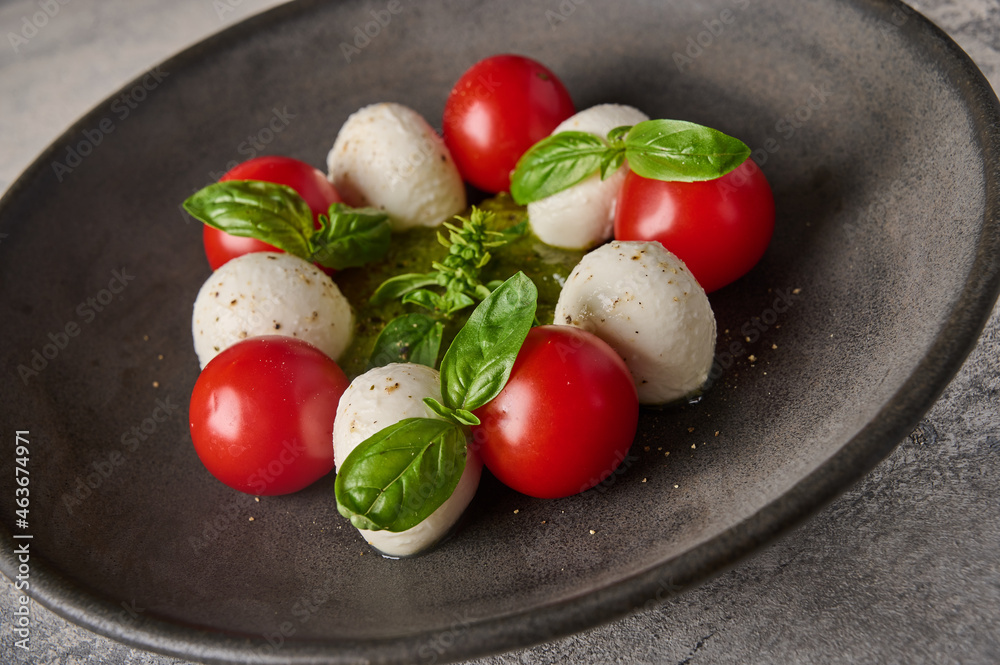 Macro italian caprese salad with ripe tomatoes, fresh basil and mozzarella cheese in black plate Macro italian caprese salad with ripe tomatoes, fresh basil and mozzarella cheese in black plate