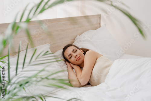 Smiling calm young woman in casual casual clothes lying in bed hands folded under head sleep rest relax spend time in bedroom lounge home in own room house wake up dream be lost in reverie good day.