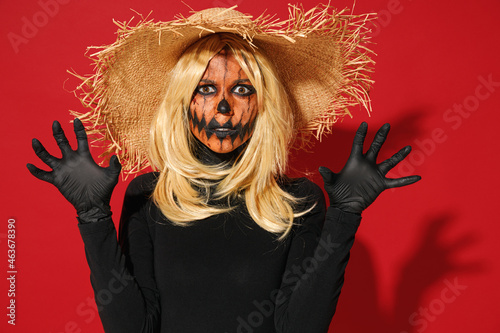 Young shcoked woman with Halloween makeup mask wearing straw hat black scarecrow costume threatening say booo isolated on plain red color background studio portrait. Celebration holiday party concept. photo