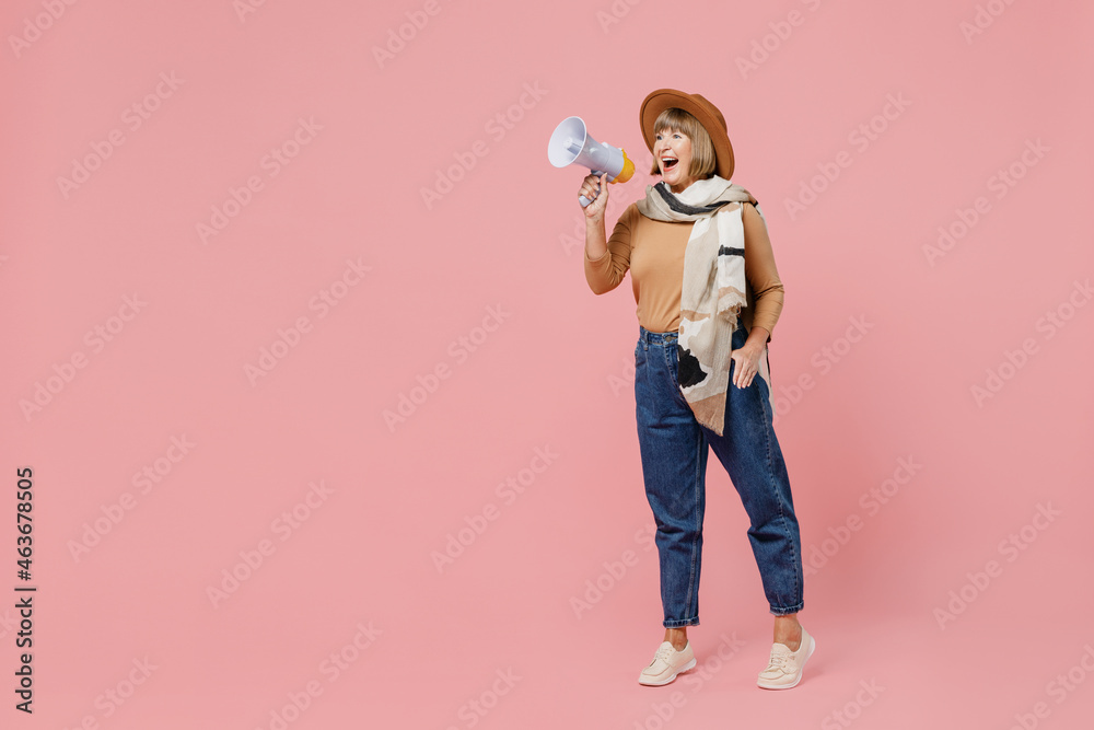 Full size body length traveler tourist mature elderly senior lady woman 55 years old wear brown shirt hat scarf hold scream in megaphone isolated on plain pastel light pink background studio portrait Full size body length traveler tourist mature elderly senior lady woman 55 years old wear brown shirt hat scarf hold scream in megaphone isolated on plain pastel light pink background studio portrait