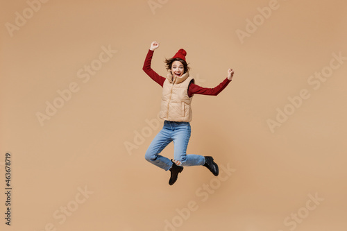 Full body overjoyed happy young woman 20s wears red turtleneck vest beret jump high do winner gesture clench fist isolated on plain pastel beige background studio portrait. People lifestyle concept. © ViDi Studio