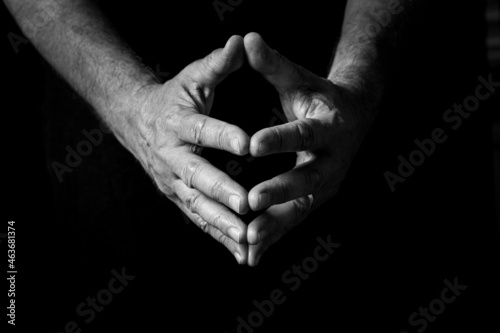 Male hands held out, clasped together in thought or prayer.