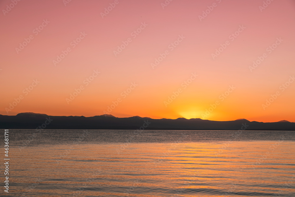 Beautiful bright sunset sky on the lake and silhouette mountains on the horizon.