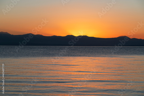  Beautiful bright sunset sky on the lake and silhouette mountains on the horizon. © Inga Av