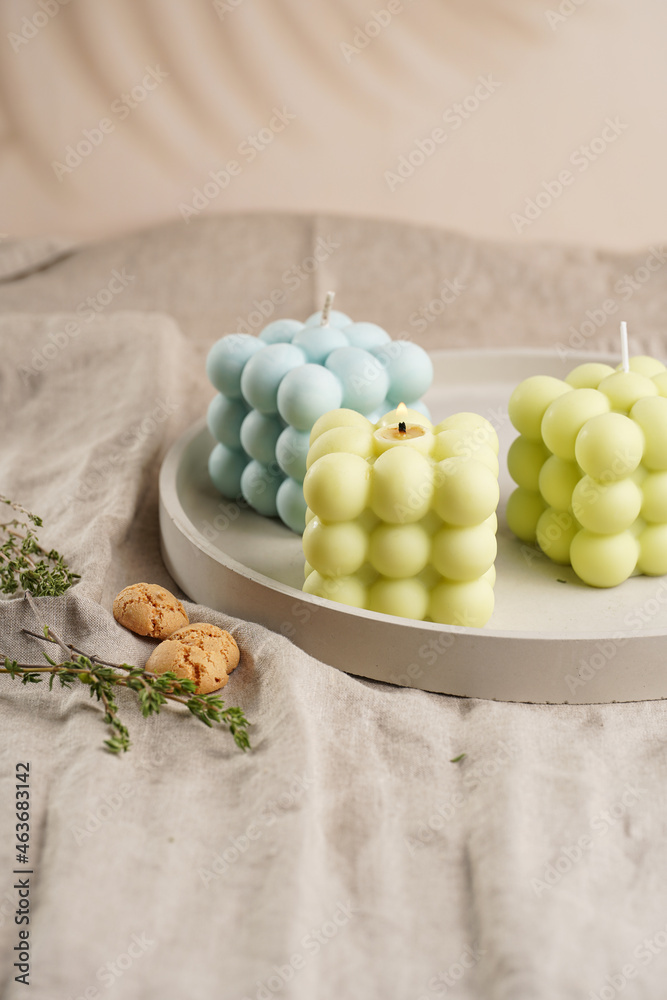 Green, blue and white square bubble candles on a concrete tray on a linen table cloth