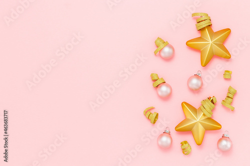 Festive background with Christmas tree decoration golden stars, golden ribbon and Christmas balls top view on pink background, copy space