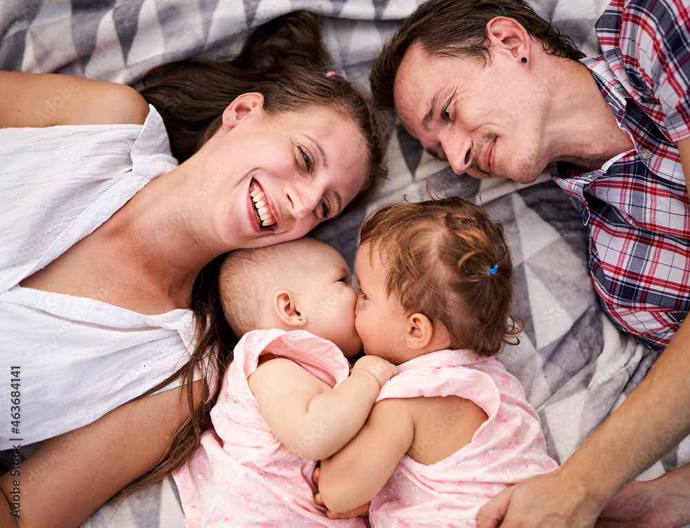 Happy family lies on a picnic blanket together - Young parents with a toddler and a baby daughter having fun - Bonding, love and care lifestyle concept from top view