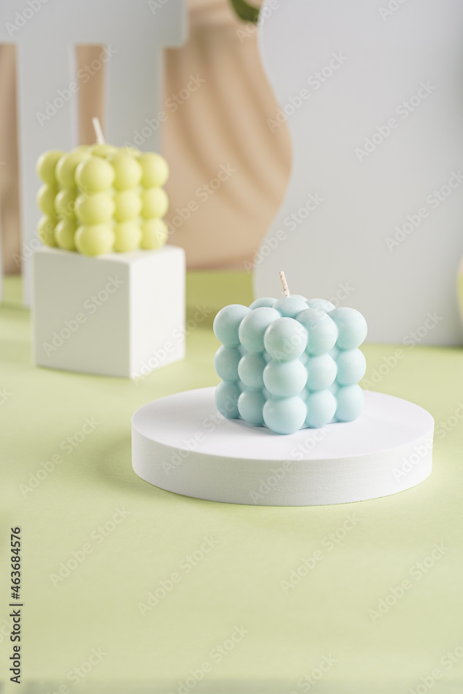 One blue square bubble candle on a white oval and an off-white candle on a cube in the back