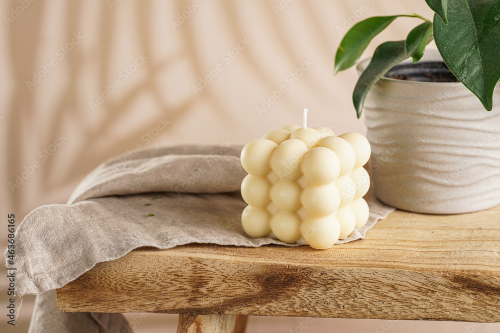 An off-white square bubble candle on a linen cloth on a rustic wooden table with plants at a tropical setting An off-white square bubble candle on a linen cloth on a rustic wooden table with plants at a tropical setting