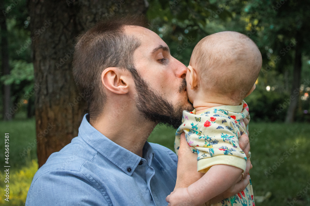 Young father holding baby son and kiss him on cheek close-up on the background of a summer landscape. Father's tenderness to his son Young father holding baby son and kiss him on cheek close-up on the background of a summer landscape. Father's tenderness to his son