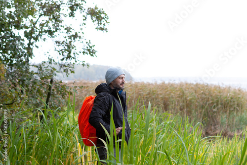 Man with orange backpack standing by the lake