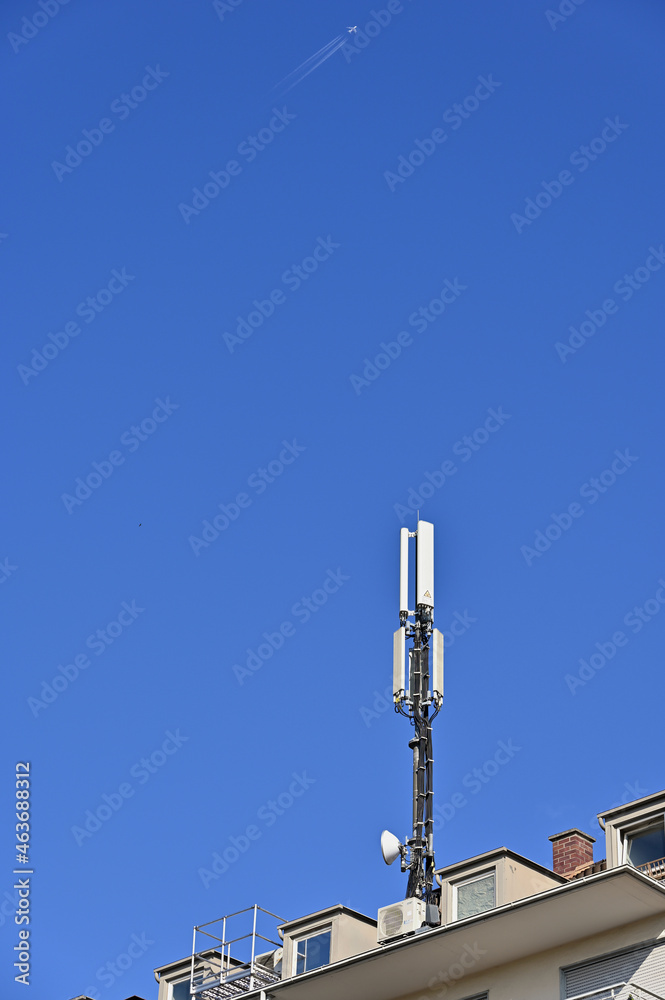 Mobilfunkantenne auf Hausdach vor blauem Himmel mit Flugzeug Mobilfunkantenne auf Hausdach vor blauem Himmel mit Flugzeug