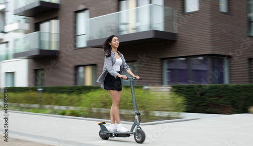 Happy young woman riding electric scooter on urban sidewalk photo