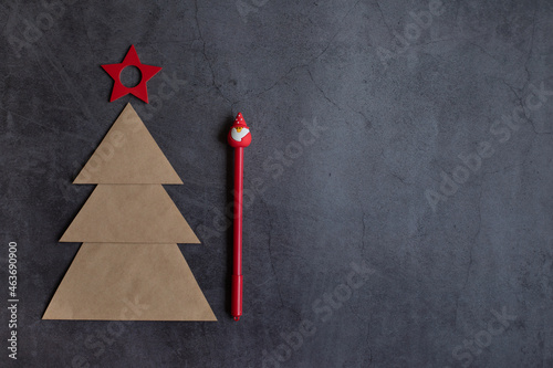 Christmas accessories on a grey background, a tree made of craft paper, a red pen in the form of Santa and star. Space for text, concept holidays.