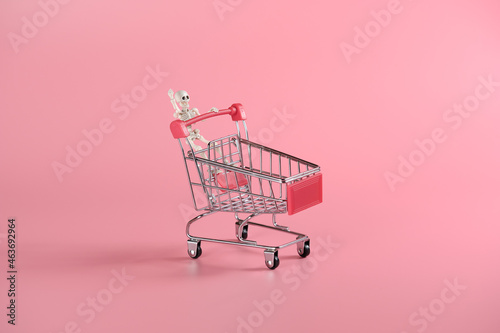 The skeleton is being rolled on a shopping trolley. Bright pink background for Halloween sale promotional material with placement for text