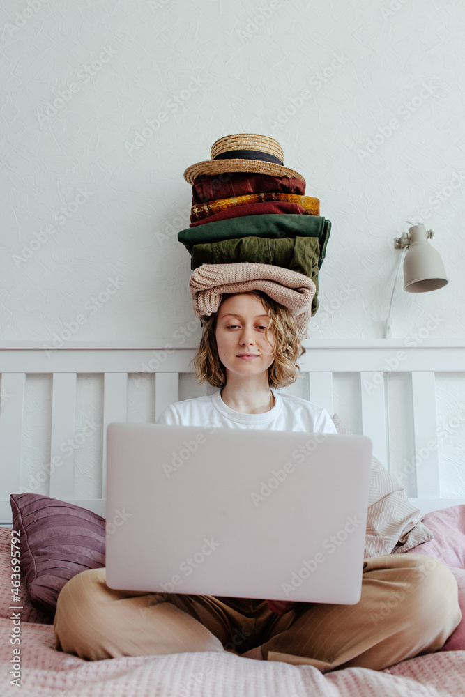 © Sergey Narevskih/Stocksy - Woman with stack of clothes using laptop