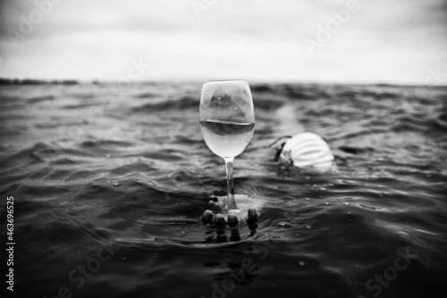 Surreal concept photography. Swimmer holding a glass of wine in the sea