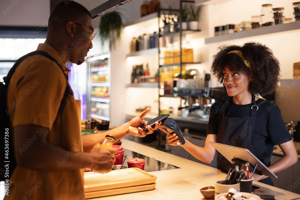 Smiling black waitress taking contactless payment on POS terminal from ...