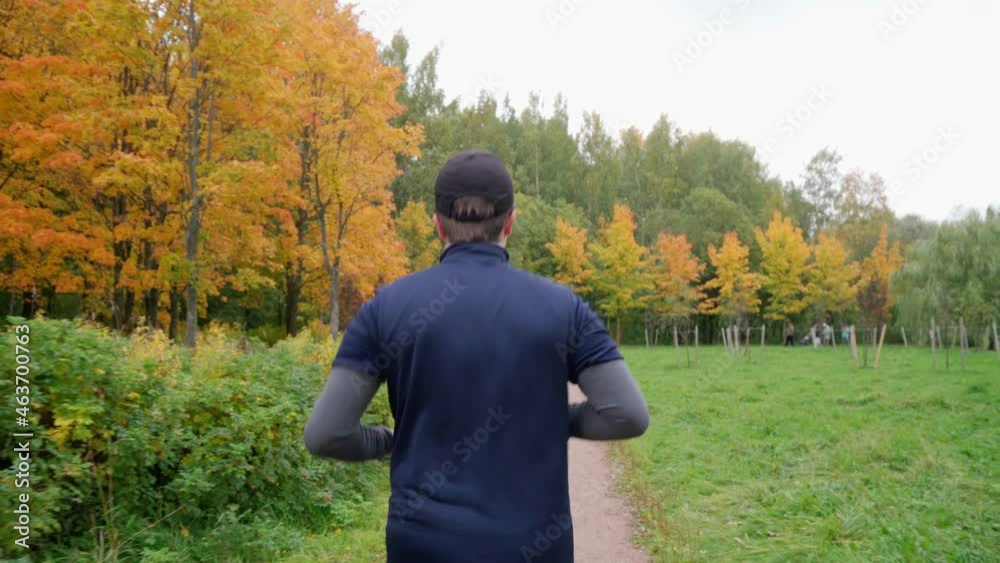 Shot from the back of a Young man running in park on public autumn background, amateur runner jogging at outdoor workout on background of orange and yellow trees. Healthy lifestyle concept. 
