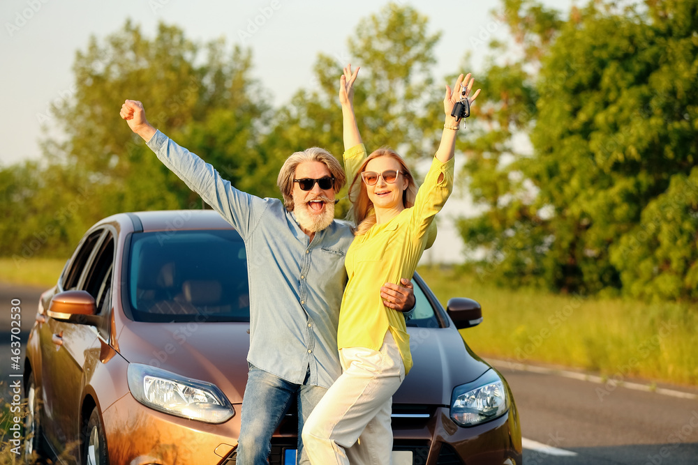 Happy mature couple with keys near car in countryside