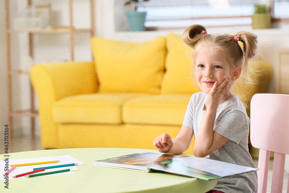 Cute little girl with ponytails reading book at table in living room Cute little girl with ponytails reading book at table in living room