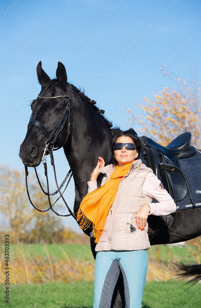 Obraz premium portrait of beautiful black horse with his owner and rider posing in green grass meadow. autumn season