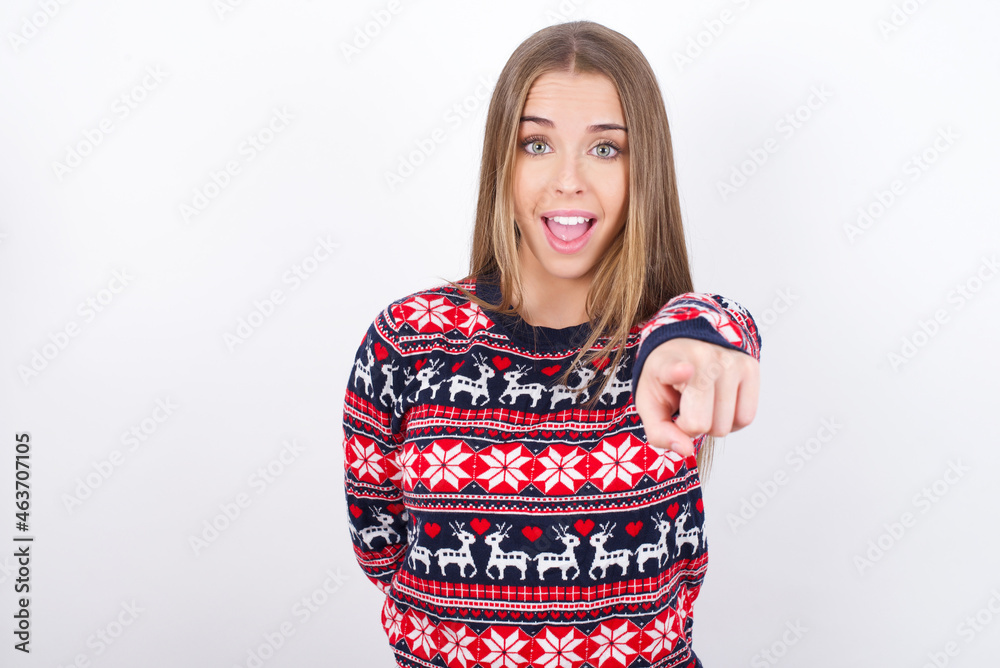 Excited positive Young caucasian girl wearing christmas sweaters on white background points index finger directly at you, sees something very funny. Wow, amazing Excited positive Young caucasian girl wearing christmas sweaters on white background points index finger directly at you, sees something very funny. Wow, amazing