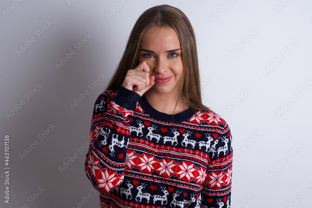 Disappointed dejected Young caucasian girl wearing christmas sweaters on white background wipes tears stands stressed with gloomy expression. Negative emotion Disappointed dejected Young caucasian girl wearing christmas sweaters on white background wipes tears stands stressed with gloomy expression. Negative emotion