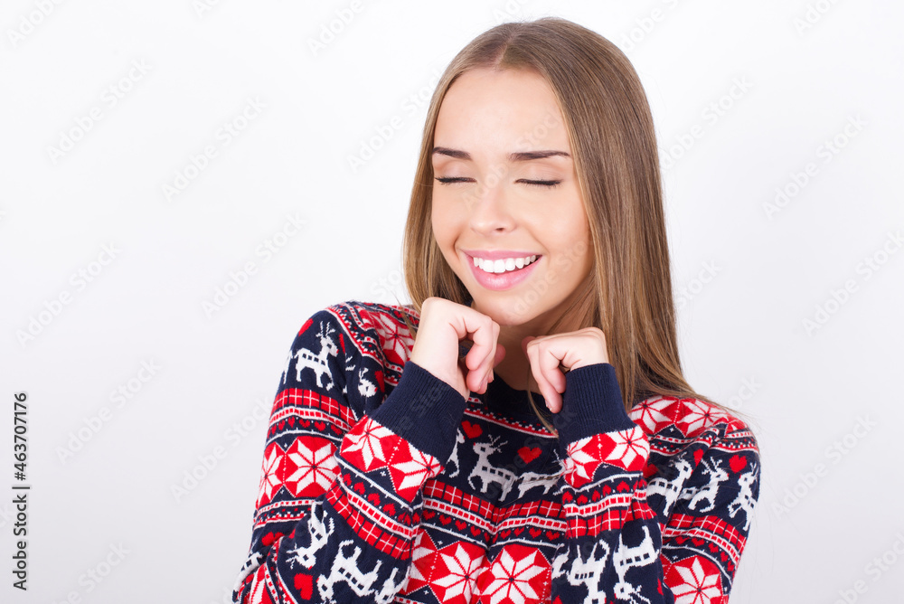 Young caucasian girl wearing christmas sweaters on white background grins joyfully, imagines something pleasant, copy space. Pleasant emotions concept. Young caucasian girl wearing christmas sweaters on white background grins joyfully, imagines something pleasant, copy space. Pleasant emotions concept.