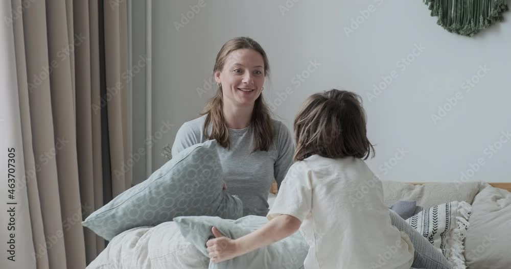 Happy kid boy playing pillow fight with smiling babysitter jumping on bed at home. Active laughing child and young woman spending time together have fun enjoying childhood motherhood parenthood Happy kid boy playing pillow fight with smiling babysitter jumping on bed at home. Active laughing child and young woman spending time together have fun enjoying childhood motherhood parenthood