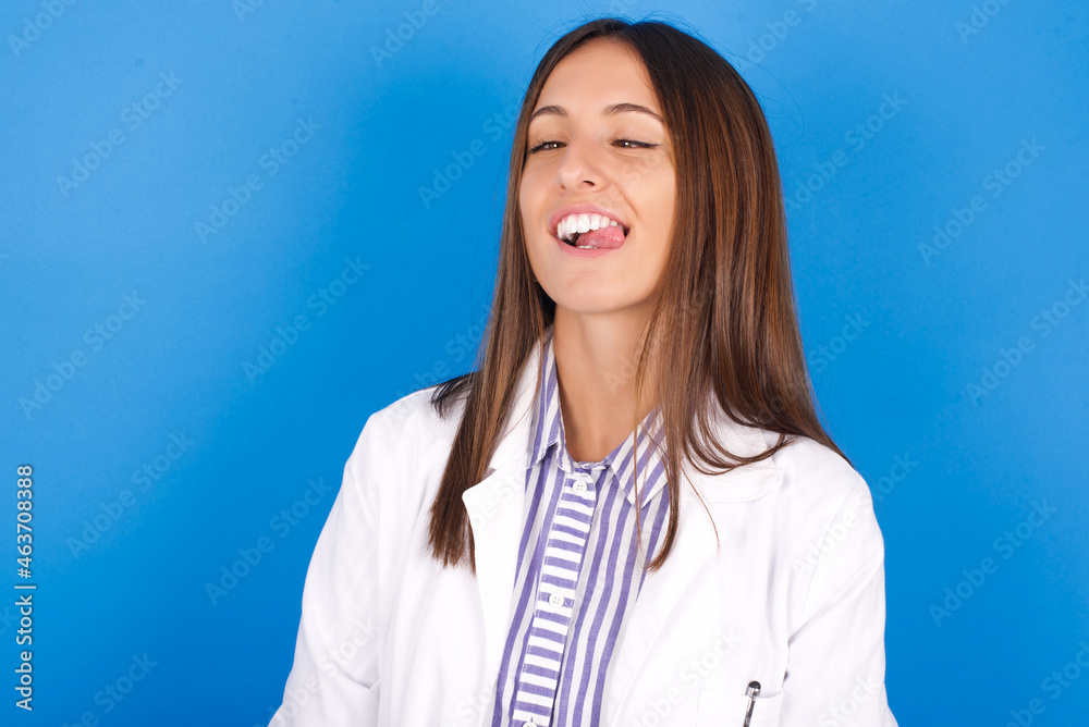 Young european doctor woman on blue background showing grimace face crossing eyes and showing tongue. Being funny and crazy Young european doctor woman on blue background showing grimace face crossing eyes and showing tongue. Being funny and crazy