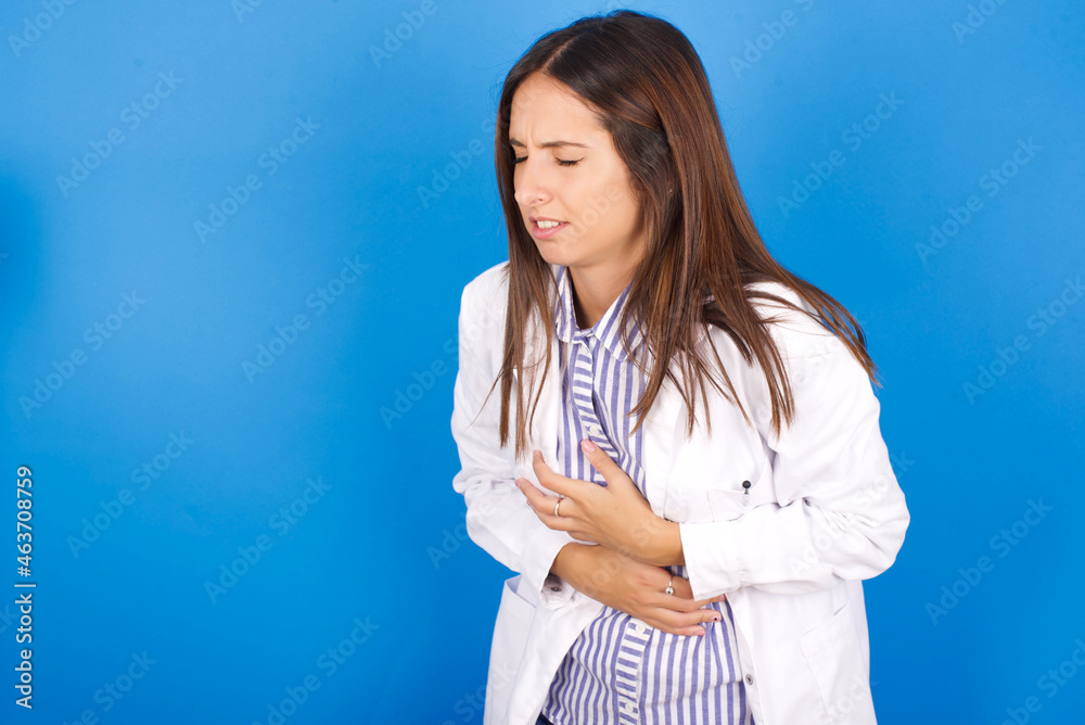 Young european doctor woman on blue background with hand on stomach because nausea, painful disease feeling unwell. Ache concept. Young european doctor woman on blue background with hand on stomach because nausea, painful disease feeling unwell. Ache concept.