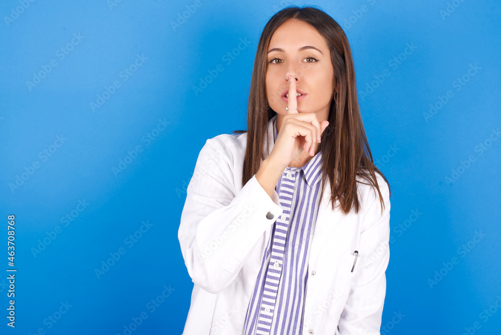 Young european doctor woman on blue background makes silence gesture, keeps finger over lips. Silence and secret concept. Young european doctor woman on blue background makes silence gesture, keeps finger over lips. Silence and secret concept.