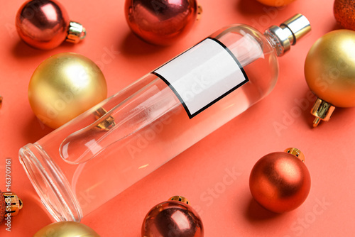Bottle of perfume and Christmas balls on red background, closeup