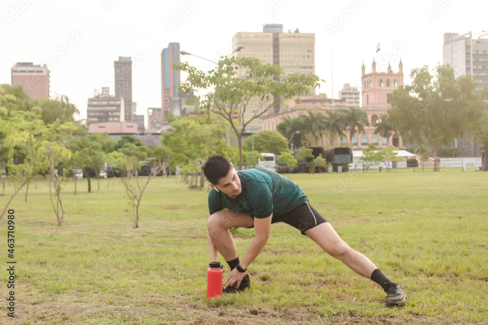 Athletic man stretching in the park with the city in the background.
