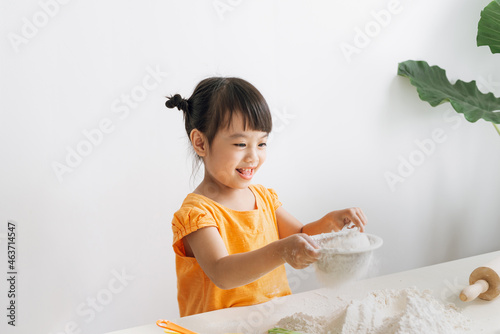 a cheerful little girl sifts flour through a sieve photo