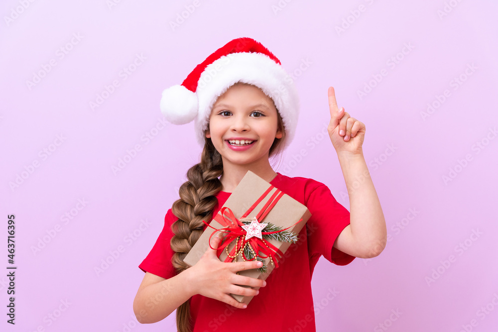 A little girl holds a New Year's gift in her hands and points her finger up. a place for advertising. A little girl holds a New Year's gift in her hands and points her finger up. a place for advertising.