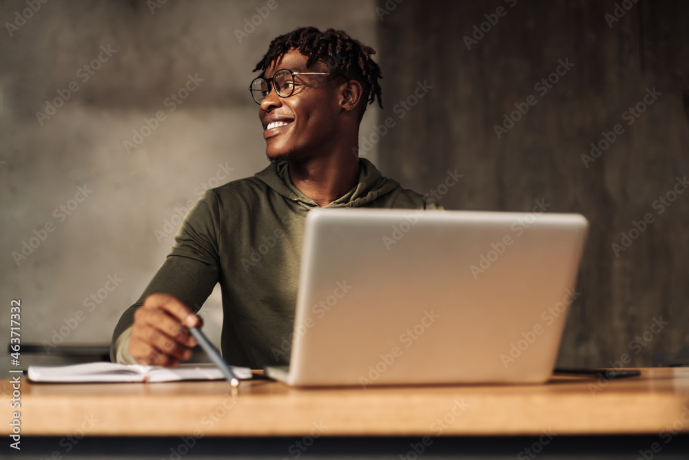 African American man with laptop and notepad at the table. a man writes with a pen in a notebook. distance learning African American man with laptop and notepad at the table. a man writes with a pen in a notebook. distance learning