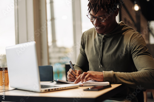 African American man with laptop and notepad at the table. a man writes with a pen in a notebook. distance learning