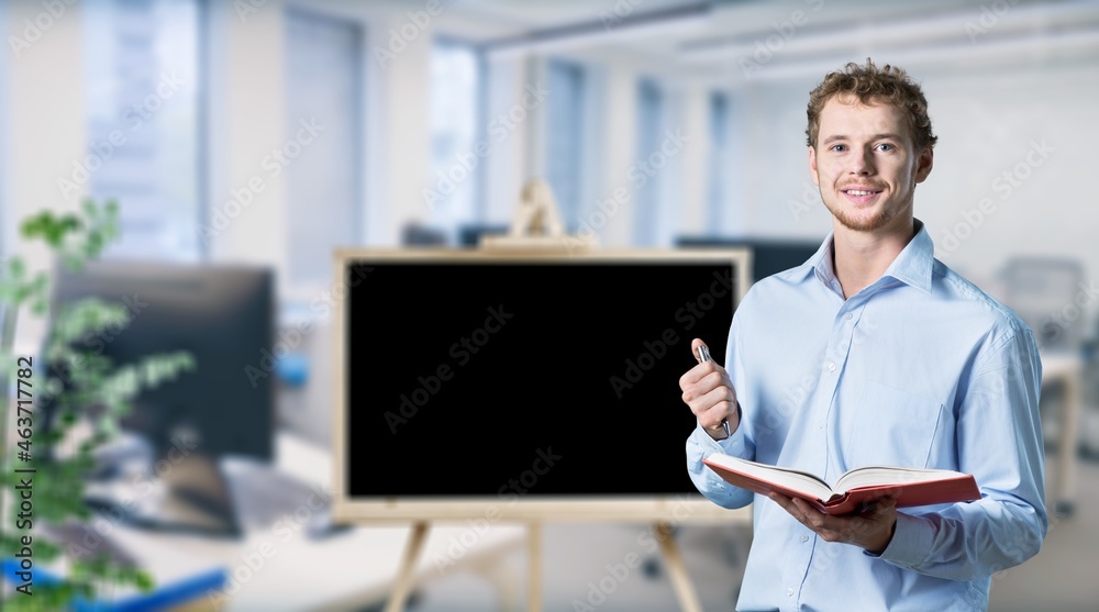 Online schooling. Positive male teacher standing near empty blackboard Online schooling. Positive male teacher standing near empty blackboard