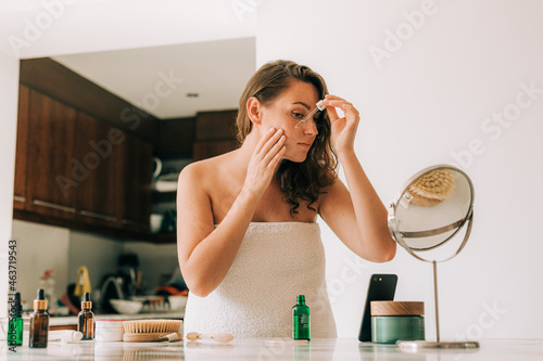 Woman using serum while looking in the mirror photo