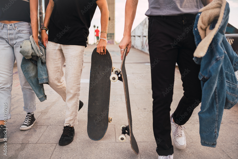 Crop?friends with skateboards walking in park Crop?friends with skateboards walking in park