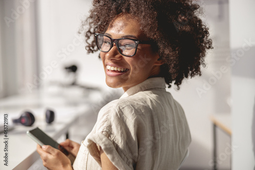 Close up of Afro American worker wearing glasses and using smartphone in the office