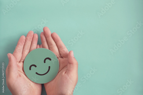 Hands holding green happy smile face paper cut, good feedback rating,positive think, customer review, satisfaction survey ,assessment, child wellness,world mental health day, Compliment Day concept photo