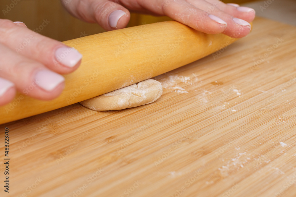 Piece of dough under a wooden rolling pin. Roll out the dough by hand.