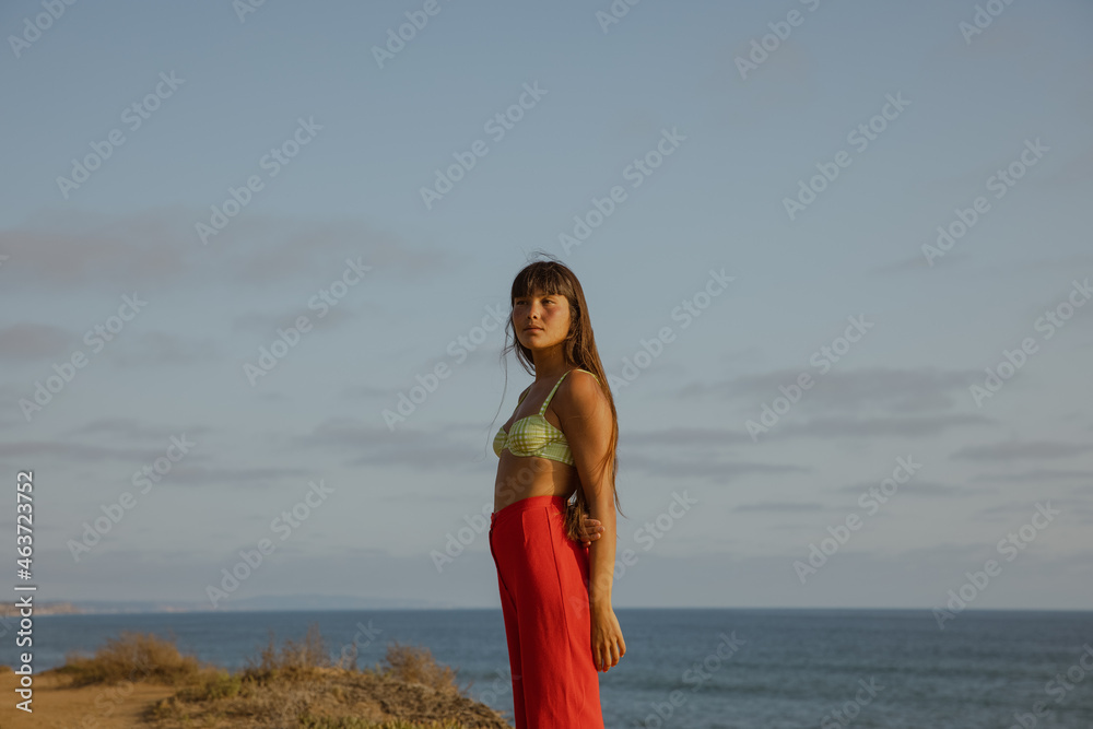 woman in red pants standing on cliff by the sea