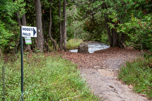 A sign pointing towards Hogg's Falls is seen beside a trail beside a river through the woods near Flesherton, Ontario. photo