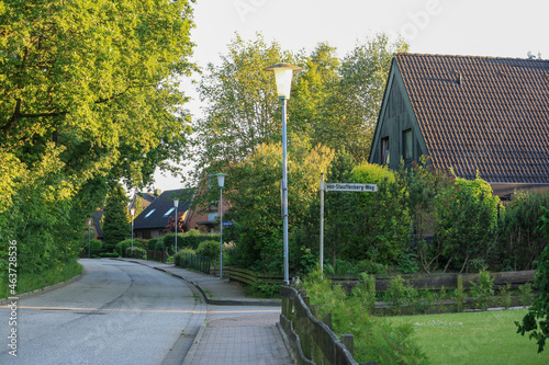 View of houses and empty road with lamp post in Itzehoe, Germany. Trees foliage and sunlight with bright summer sky background. No people.