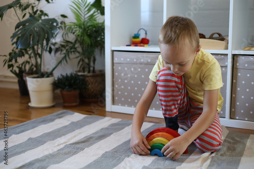 Boy plays and assembles puzzle of colored wooden geometric shapes at Montessori school. Home education